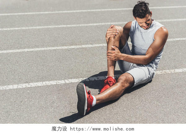 腿部受伤的年轻跑步者坐在跑道上